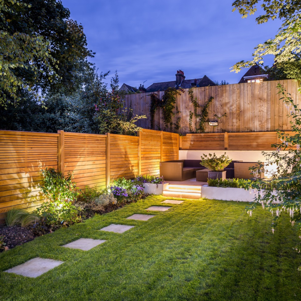 Garden at dusk with lawn, stepping stones, raised planting beds and lighting